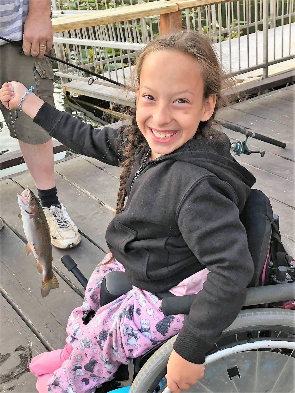 Young girl in wheelchair beaming with a fish she caught at Agur Lake Camp's accessible fishing dock